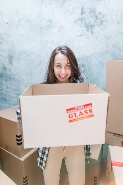 A professional removal specialist from Removals Richmond, wearing a navy blue T-shirt with a company logo and dark trousers, is inside an unfurnished room with light-colored walls and wooden flooring,